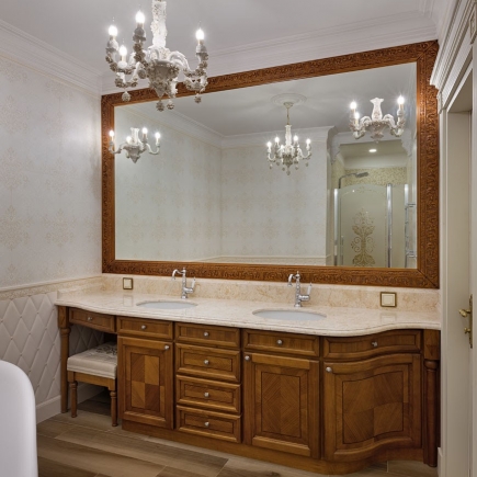 Bathroom double vanity with a large carved wood mirror frame and crystal sconces