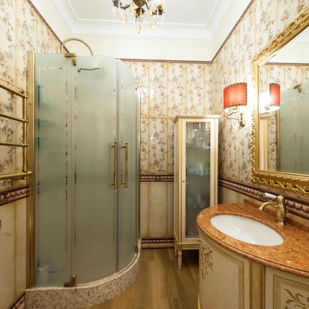Bathroom with a curved glass shower enclosure, floral wallpaper, and gilt-framed mirror