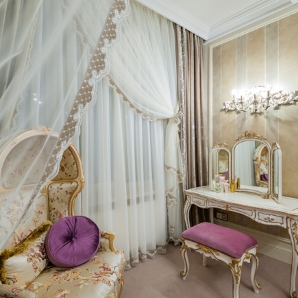 Bedroom seating nook with a canopy drape, upholstered armchair, and vanity table