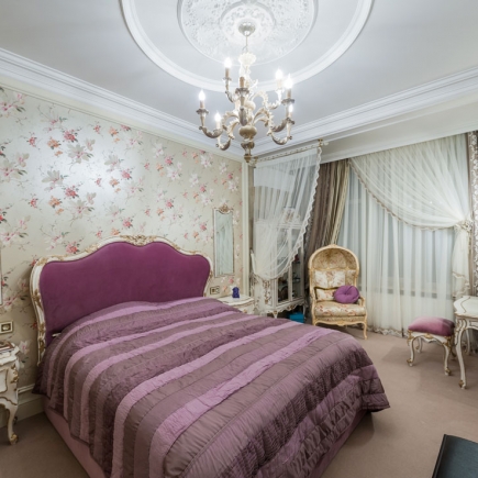 Bedroom with floral wallpaper, a tufted purple velvet headboard, and matching bedding