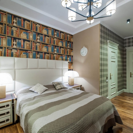 Bedroom with library-print wallpaper, tufted headboard, and matching nightstand lamps