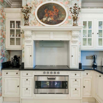 Carved wood range hood mantel topped with an oval floral painting and bronze candelabra