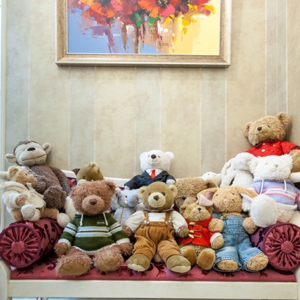 Collection of stuffed animals arranged on an upholstered bench beneath a framed painting