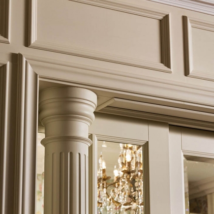Detail of carved crown molding and column capital beside a mirrored door