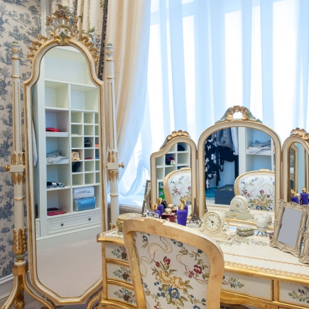 Dressing table with a gilt-framed mirror, tri-fold vanity mirror, and floral upholstered chair