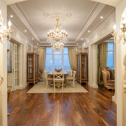 Formal dining room framed by an arched doorway with a crystal chandelier, floor-to-ceiling windows, and matching display cabinets