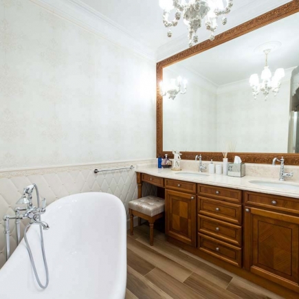 Freestanding clawfoot tub beside a carved wood vanity with a large framed mirror
