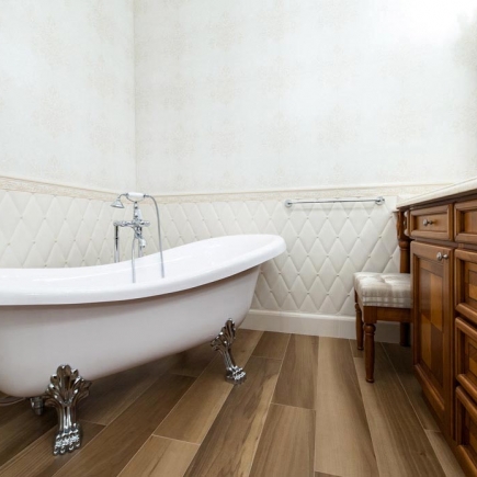 Freestanding clawfoot tub on wood flooring beside a quilted accent wall
