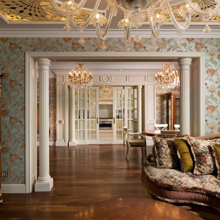 Living room framed by fluted columns with crystal chandeliers and a view into the kitchen beyond