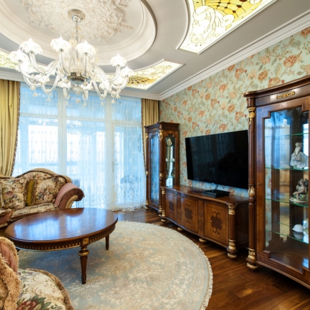 Living room with stained-glass ceiling panels, floral wallpaper, and a display cabinet beside the TV