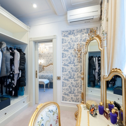 Walk-in closet with hanging garments beside a gilt-framed floor mirror and dressing table