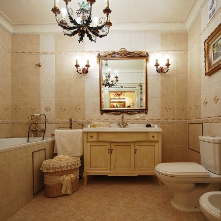 Classical bathroom with beige tile, a vanity cabinet, gilt-framed mirror and a chandelier