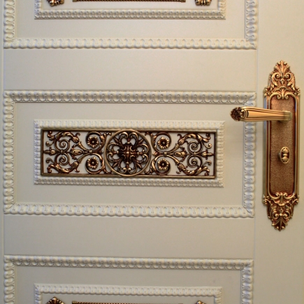 Close-up of a white panelled door with a gilded filigree grille insert