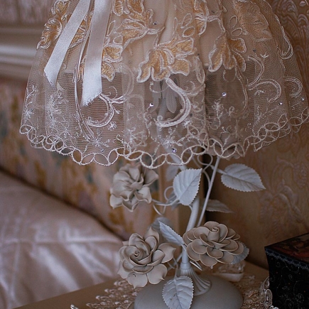 Mirrored vanity with a floral chair beneath a white porcelain-rose chandelier