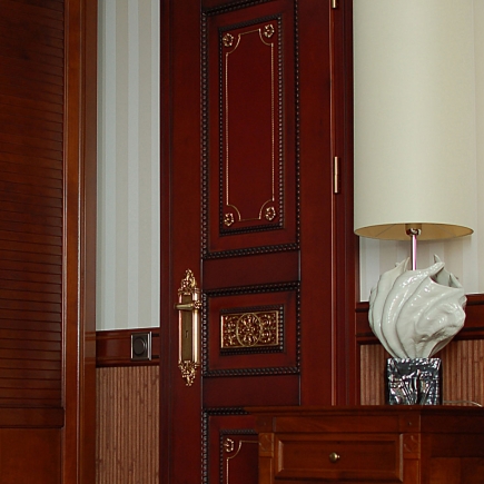 White interior door with gilded grille panels and an ornate brass handle
