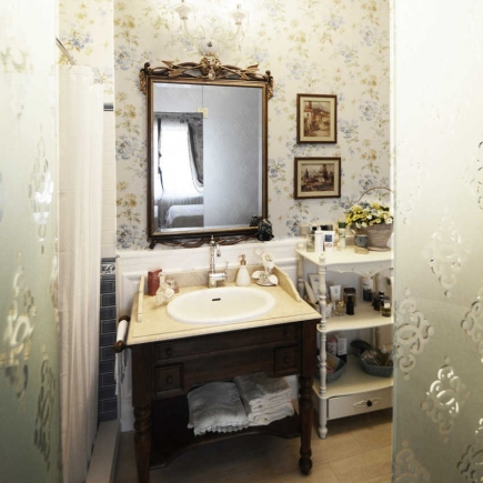 Bathroom vanity with a gilt mirror, dark wood cabinet, and floral wallpaper