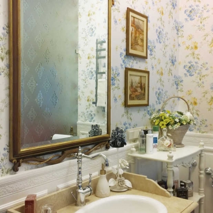 Bathroom vanity with a gilt mirror, floral wallpaper, and a basket of fresh flowers