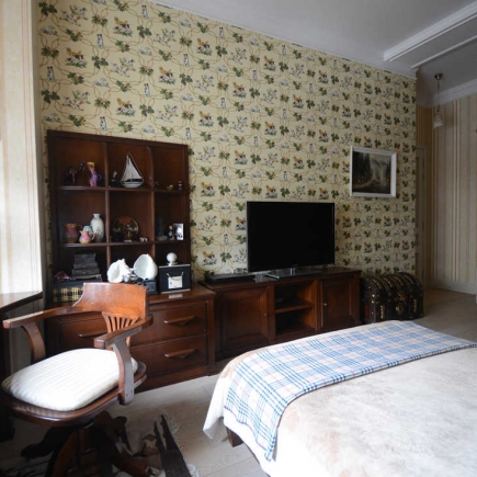 Bedroom with botanical wallpaper, a wall-mounted TV, and a plaid throw on the bed