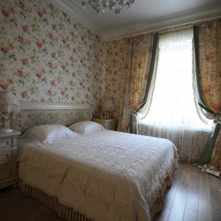 Bedroom with floral wallpaper, a lace-shaded table lamp, and a crocheted white bedspread