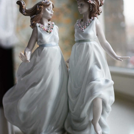 Close-up of porcelain figurines of two women in flowing gowns on a windowsill