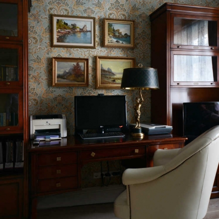 Home office nook with a mahogany desk, framed landscape paintings, and a brass desk lamp