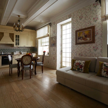 Kitchen and dining nook beneath a wrought iron chandelier, with floral wallpaper and sofa beyond