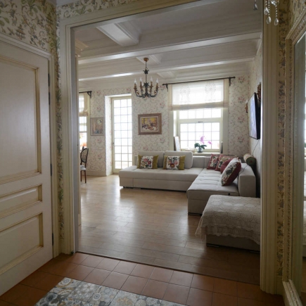 Open living room with a beige sectional sofa and floral wallpaper, viewed through the entry hall