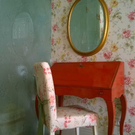 Vanity nook with a red writing desk, floral chair, and gilt oval mirror
