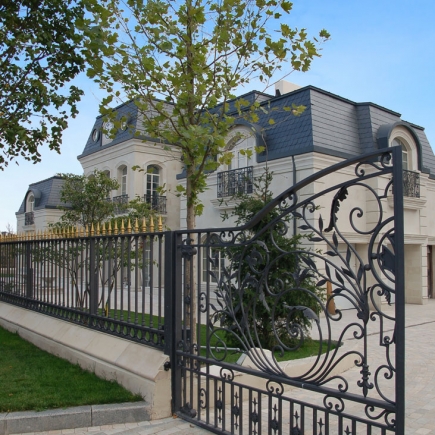 Exterior view of the mansion behind wrought-iron fencing and a mature tree