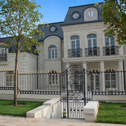 Front exterior with slate mansard roof, wrought-iron fence, and gate opening onto the entrance courtyard