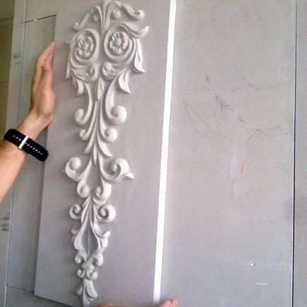 Hand-carved stone panel with floral scroll motif being fitted to the facade