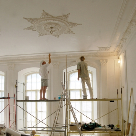 Craftsmen applying decorative plaster molding to the ceiling medallion and cornices