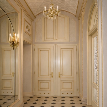 Gilt-trimmed paneled corridor with a crystal chandelier and checkerboard marble floor
