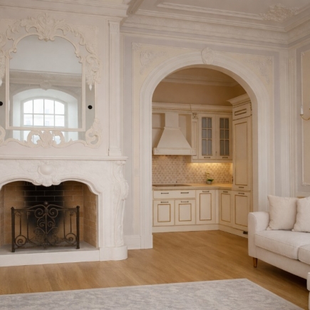 Living room with an ornate white marble fireplace opening onto the kitchen through an arched doorway