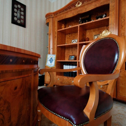 Burl-wood executive desk beside an ornate glass-front bookcase and tufted leather armchair