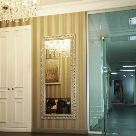 Corridor with a gilt-framed mirror reflecting a leather armchair beside a glass office door