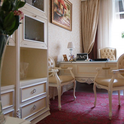 Cream-toned office with tufted armchairs, a carved desk, and a rich burgundy rug