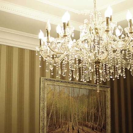 Crystal chandelier beside a framed forest landscape painting