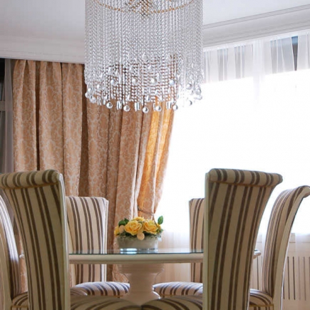 Crystal chandelier over a glass dining table with striped upholstered chairs and floral curtains