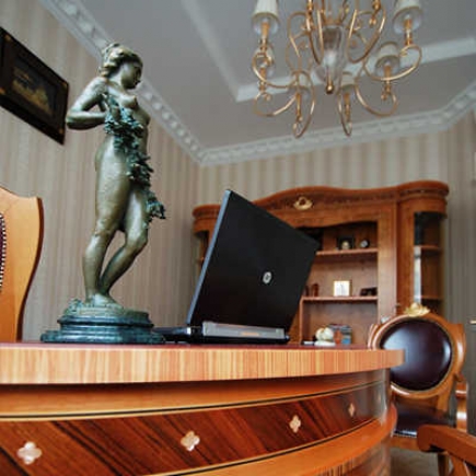 Director's desk with a bronze nymph statue and open laptop beneath a crystal chandelier