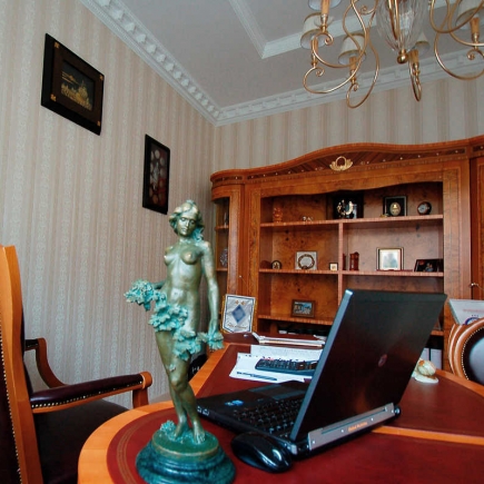 Director's office with a bronze nymph statue, laptop, and ornate burl-wood bookcase