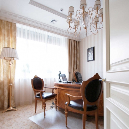 Wood-paneled office with a gold chandelier, leather chairs, and a floor lamp by the window