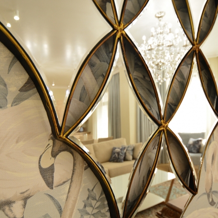 Close-up of a diamond-shaped mirror panel reflecting the living room and chandelier