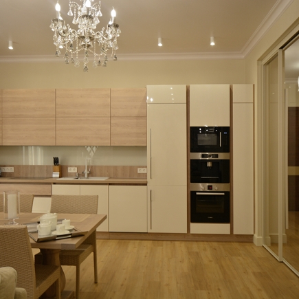 Light oak kitchen with a crystal chandelier, glossy cream cabinetry, and built-in appliance tower
