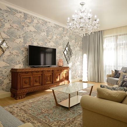 Living room with flamingo-print wallpaper, antique carved sideboard, and glass coffee table