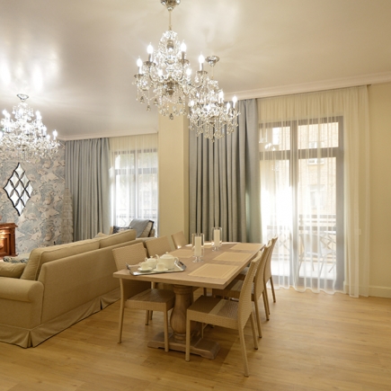 Open dining and living area with layered crystal chandeliers and floor-to-ceiling sheer curtains