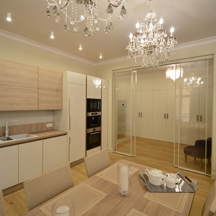 Open kitchen and dining area framed by a glass sliding partition beneath twin crystal chandeliers