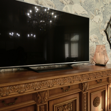 Wall-mounted TV on the antique carved sideboard against flamingo-print wallpaper
