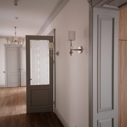 Corridor with an open lattice-glass door, twin wall sconces and a chandelier beyond