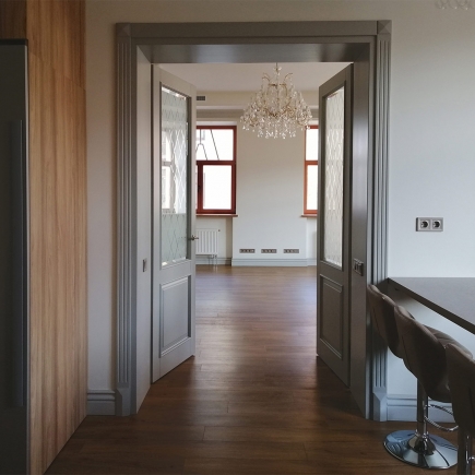 Welcoming guests between open lattice-glass double doors beneath a crystal chandelier